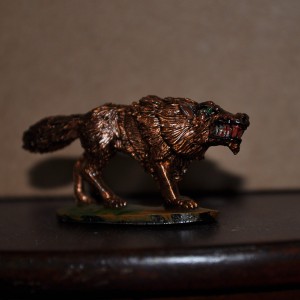 A brass colored wolf miniature with green eyes and blood-drenched teeth