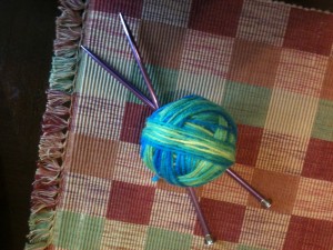 A ball of blue, green, and yellow yarn with two knitting needles crossed under it
