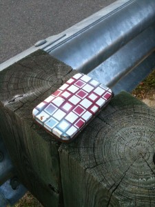 A colorful metal tin box, closed, on the wooden support beam of a bridge guardrail