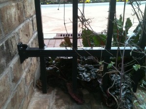 A wroght iron fence bolted to a brick wall near some plants
