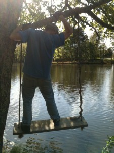 A man climbs on a tree swing by a lake